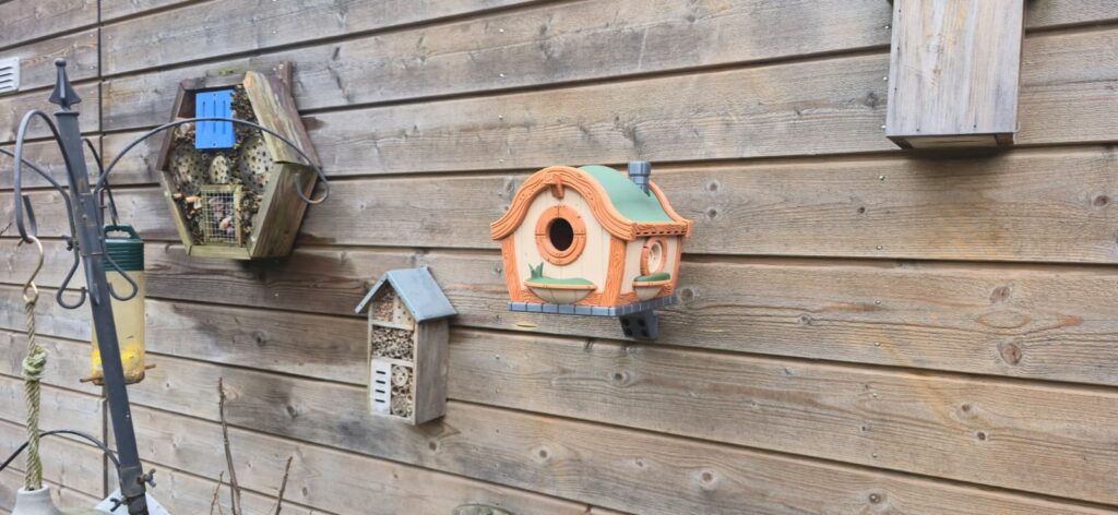 Kleurrijk vogelhuisje bevestigd aan de houten wand van een schuur / Colourful birdhouse mounted on a wooden shed